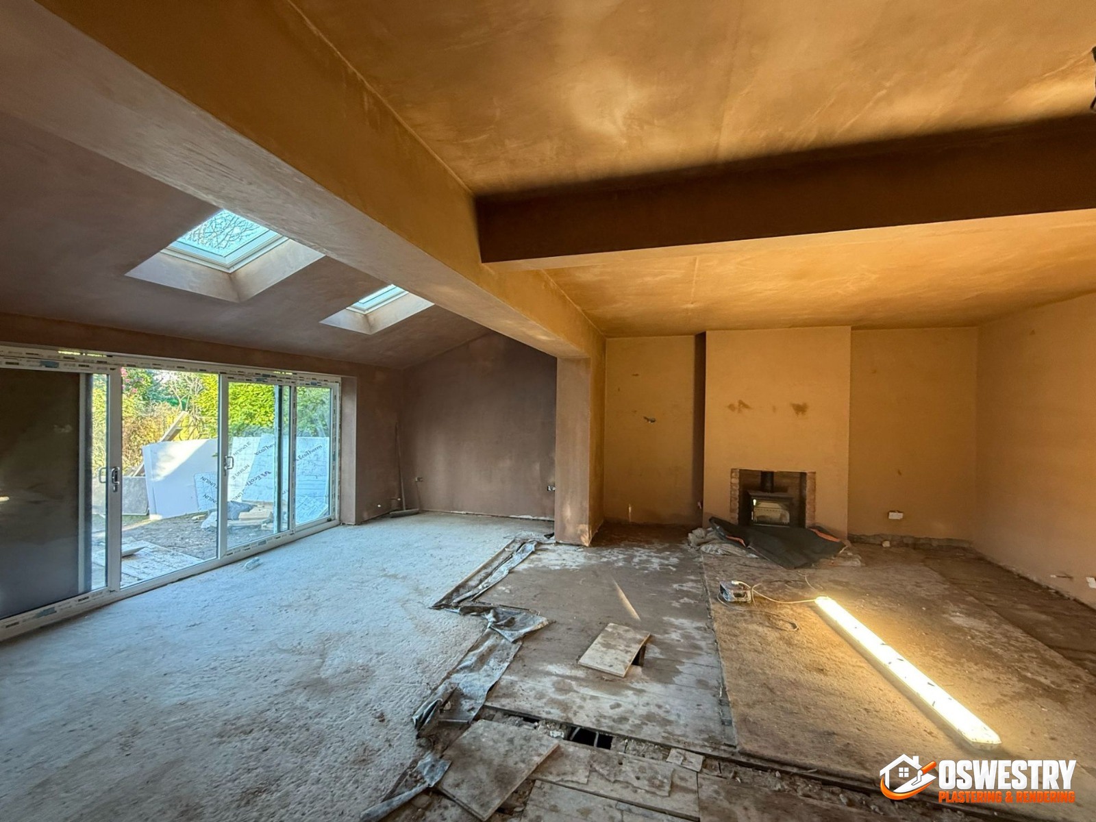 Open-plan UK extension interior freshly bonded and skimmed by Oswestry Plastering & Rendering — walls, ceilings and structural beams finished smooth with pink plaster, bi-fold doors and roof lanterns in place